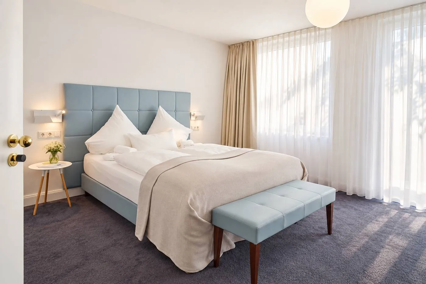 Zimmer im Maison Marsil mit hellblauem Bett, Polsterbank und bodentiefen Fenstern